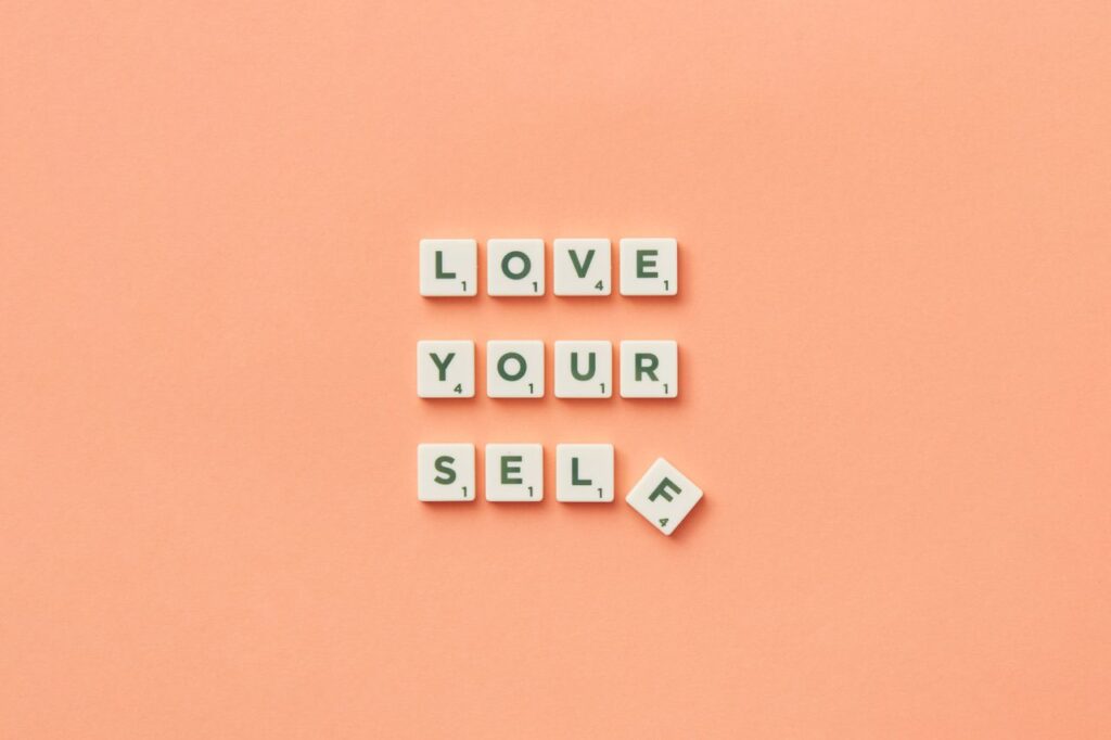 Scrabble tiles spelling 'Love Yourself' on a peach background, inspiring self-care.