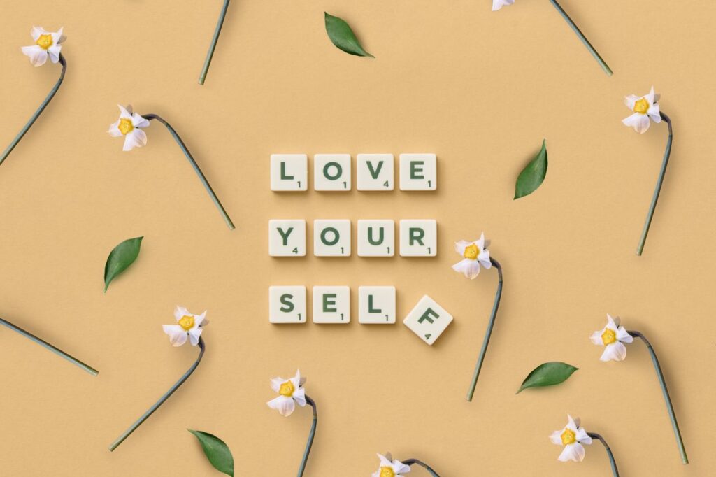 The Art of Drawing Readers In: Your attractive post title goes here Scrabble tiles spelling 'Love Yourself' surrounded by flowers and leaves on a flat surface.